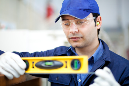 Una persona che indossa occhiali di sicurezza, un berretto blu e guanti utilizza una livella a bolla per la misurazione.