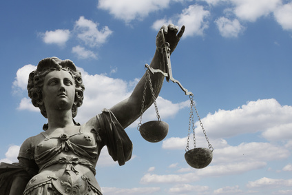 Eine Statue von Lady Justice, die die Waage der Gerechtigkeit vor einem blauen Himmel mit Wolken hält.